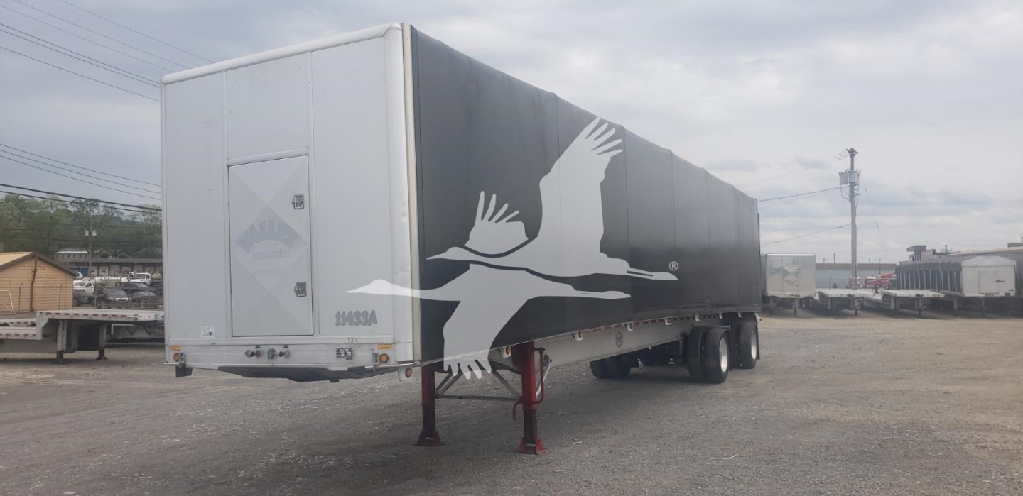 Curtainside trailer with white front and black side panels featuring a large flying crane silhouette and red landing gear legs visible.