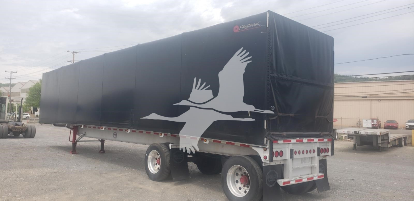 Curtainside trailer showing black tarp with white bird graphic and rear LED lights, side view.