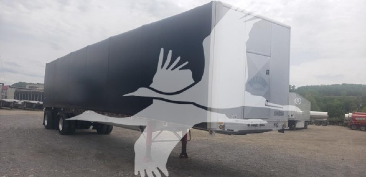 Curtainside trailer showing large white bird silhouette graphic on black side with hitch and landing gear visible.