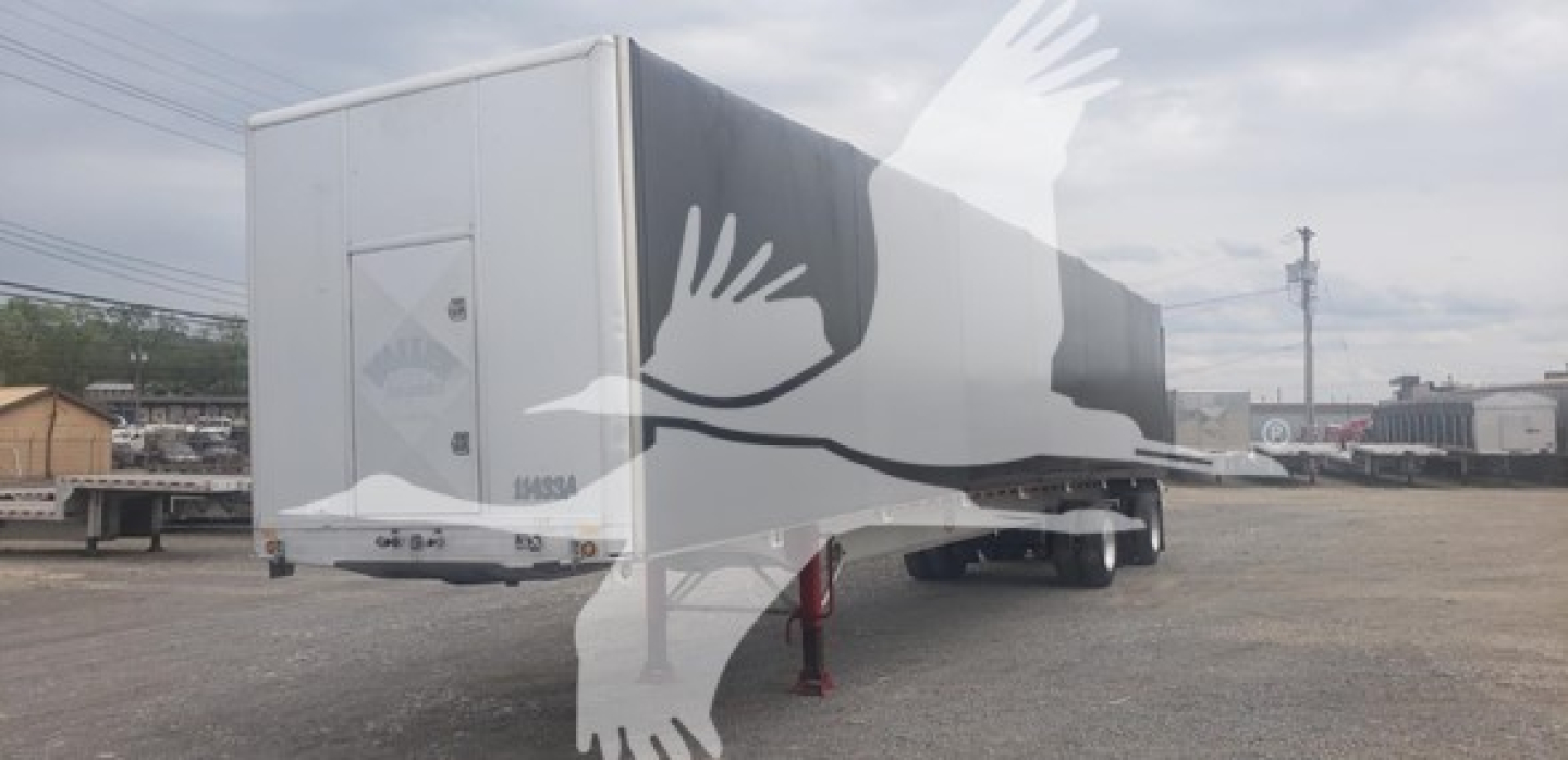 Trailer in a lot, side and rear views visible with black and white curtain side. Appears to be a Mac flatbed trailer with a rear door and support legs.