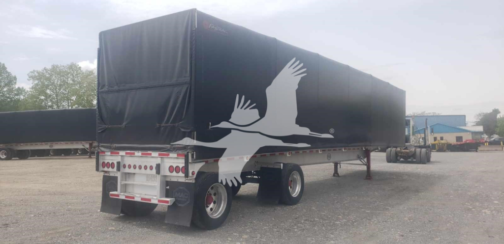 Trailer showing curtainside cargo bed with black tarp and white graphic birds, dual rear wheels, in outdoor yard.