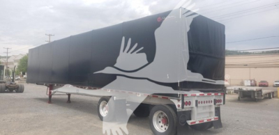 Curtainside trailer with large white bird graphic on black cover, viewed from rear-left side showing trailer and wheels.