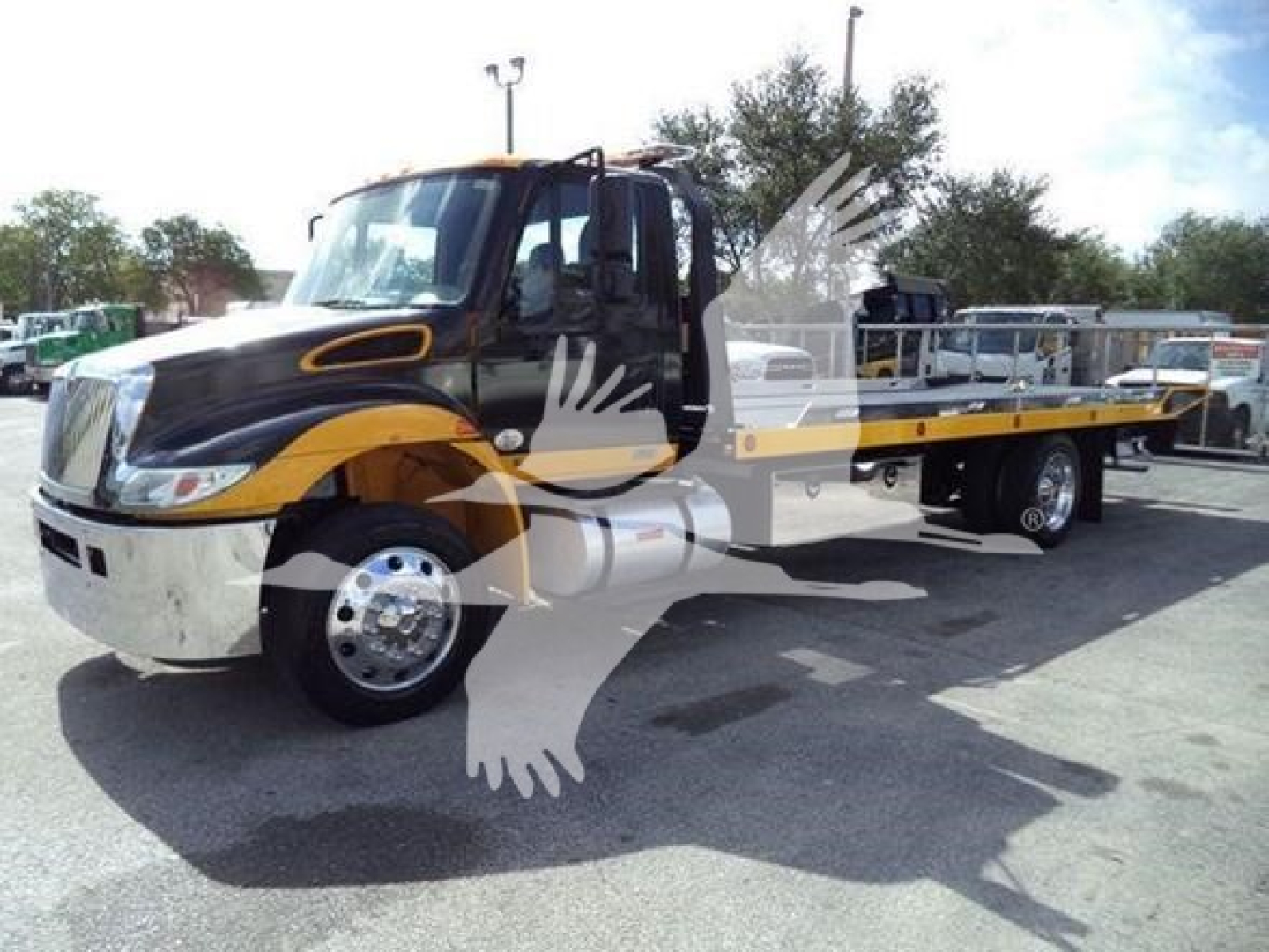 Flatbed tow truck in black and yellow livery parked in lot with long flatbed, cab doors open, International Durastar branding not visible.