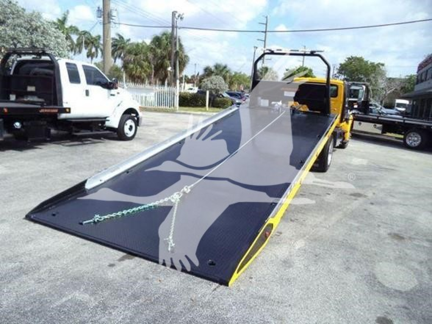 2019 International Durastar 4300 rollback tow truck with a lowered metal ramp bed; yellow and black colors; VIN plate and stock info not legible; other trucks in background.