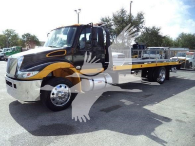 Flatbed tow truck in black and yellow livery parked in lot with long flatbed, cab doors open, International Durastar branding not visible.