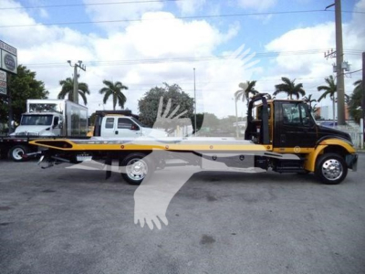 Volvo? No. A 2019 International Durastar 4300 rollback tow truck with a long flatbed, black cab and yellow/Brown body, side view showing towing chassis and wheels.