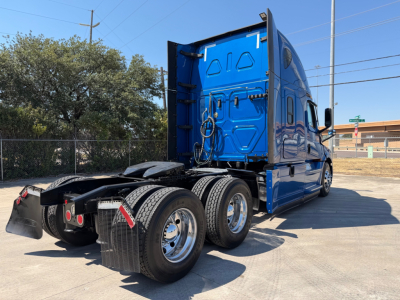 Truck chassis and blue Freightliner sleeper cab from rear-left view showing dual rear axles and fifth wheel area.