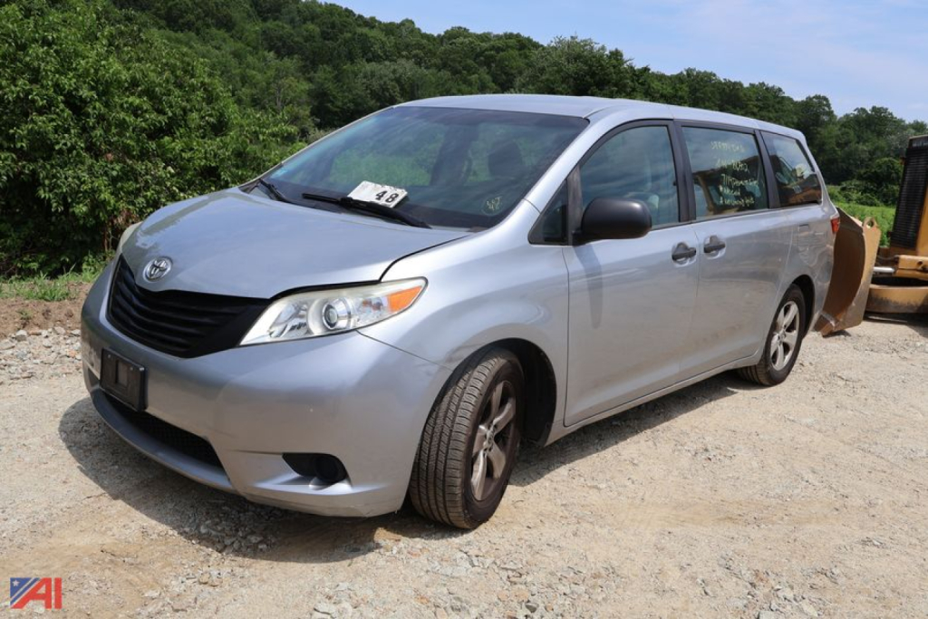Toyota Sienna minivan in a light blue/silver color, front-left view, with a paper on the windshield and a construction area in the background.