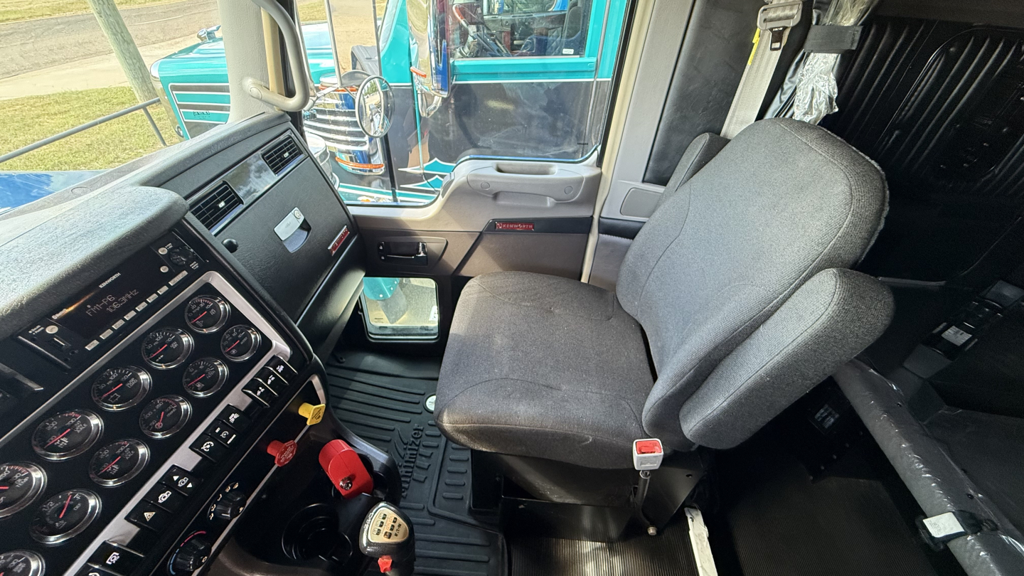 Kenworth W900 truck cab interior showing driver seat and dashboard with multiple gauges and controls.