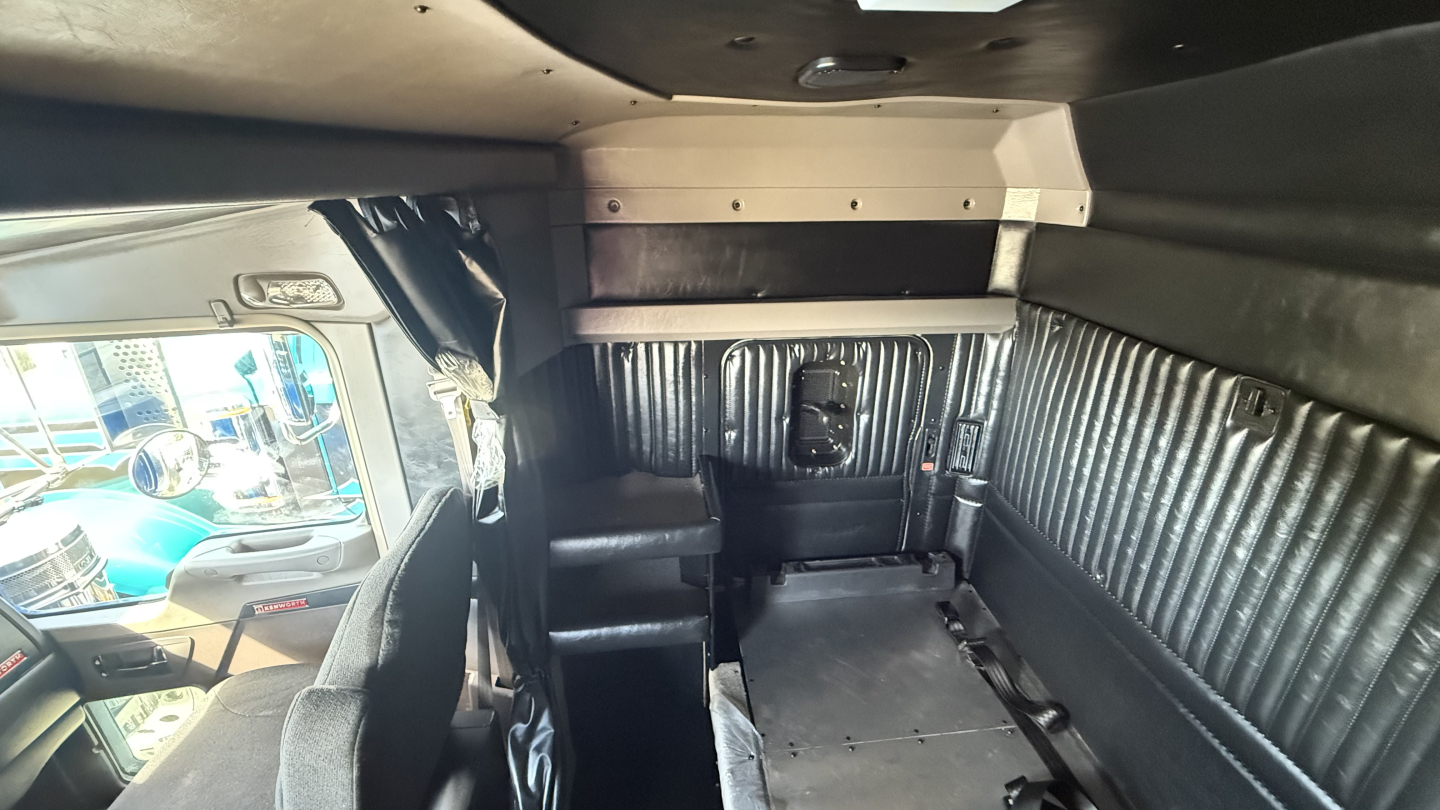 Kenworth W900 truck cab interior with sleeper area and side window, showing rear cargo area and partition.
