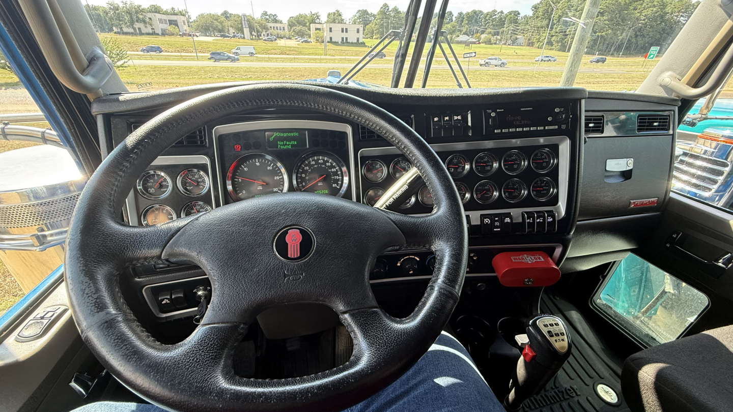 Kenworth W900 truck interior dashboard and steering wheel with multiple gauges and controls.