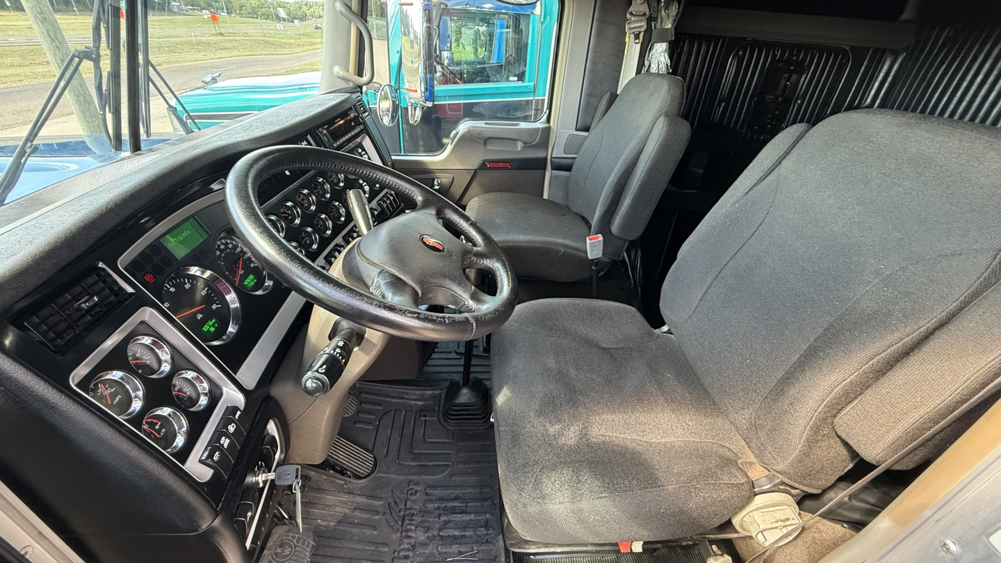 Kenworth W900 truck interior view showing steering wheel, dashboard gauges, driver's seat, and passenger seat.