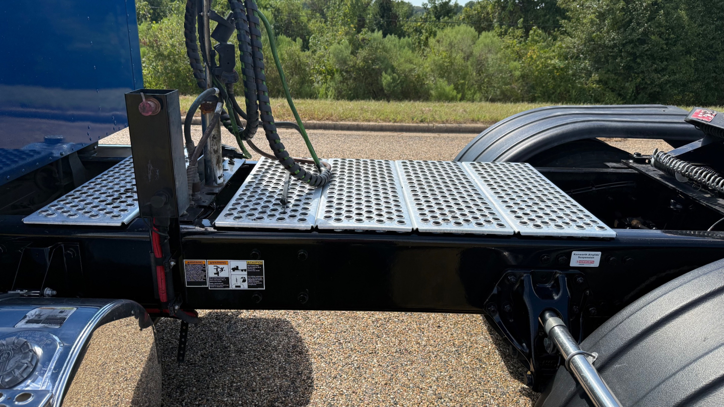 Kenworth W900 sleeper-conventional truck chassis showing platform and rear cab area with hydraulic lines and connection plate.