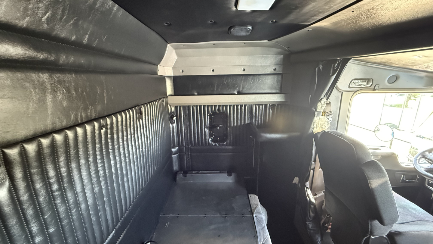 Kenworth W900 sleeper cab interior showing side panels and seating area with black upholstery and overhead lighting.