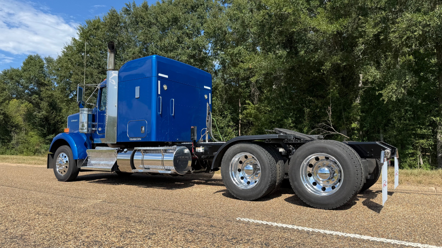 Kenworth W900 tractor cab with blue sleeper, dual rear wheels, side view showing chrome exhaust stack and blue paint; no visible branding text on image.