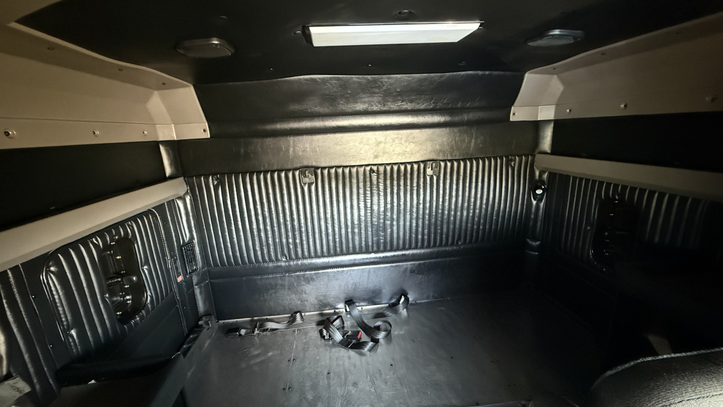 Kenworth W900 truck cargo area showing rear sleeper alcove and metal ribbed walls with harnesses on floor.
