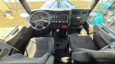 Kenworth W900 cab interior with steering wheel, dashboard, and two bench seats visible from cabin perspective.