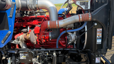 Kenworth W900 truck engine bay showing red engine block, silver exhaust manifold, blue hoses, and black radiator support. Visible labels and hoses.