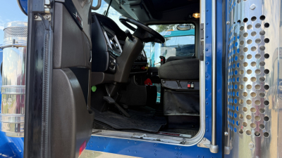 Kenworth W900 truck interior viewed from open driver door showing seat, steering wheel, and dashboard.
