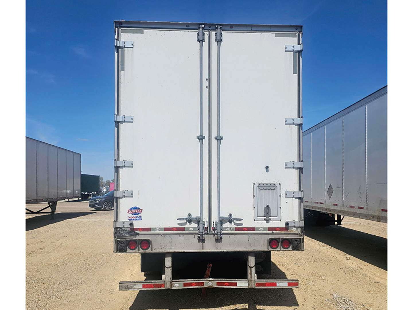 Back view of a white Utility 4000D-X trailer with double rear doors, rear bumper, and taillights in a trailer yard.