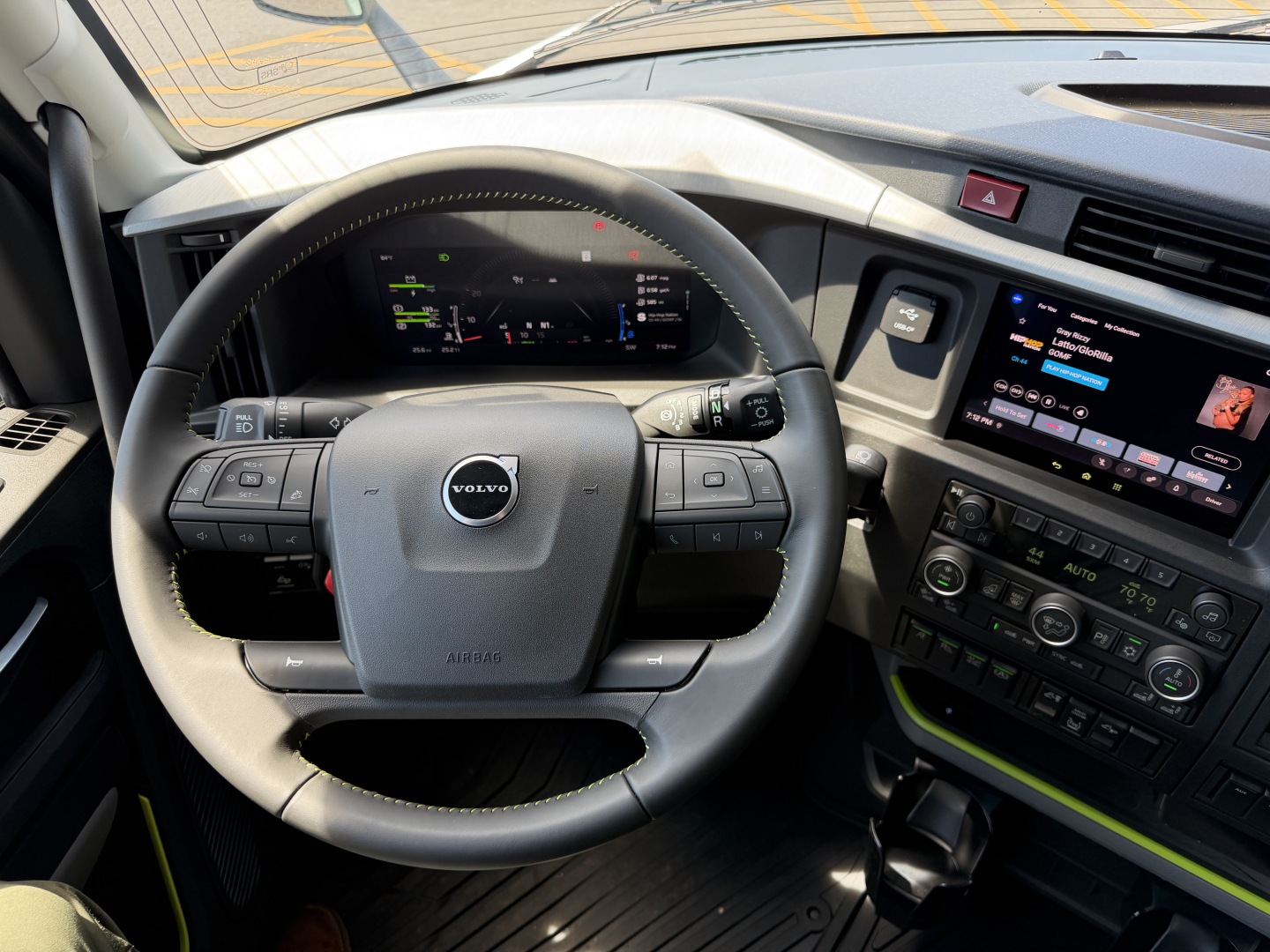 Volvo truck interior steering wheel and dashboard with digital gauge cluster and touchscreen infotainment system; visible text on screen and buttons.