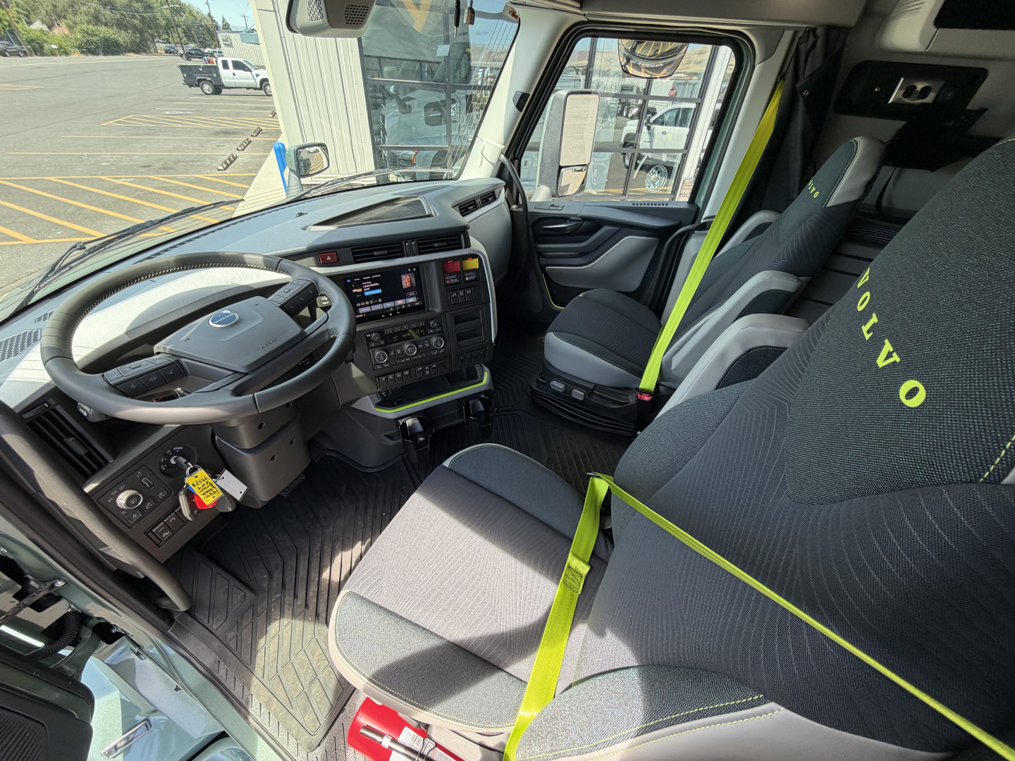 Volvo truck cab interior showing steering wheel, dashboard, driver seat with green seat belt, and passenger seat in view.