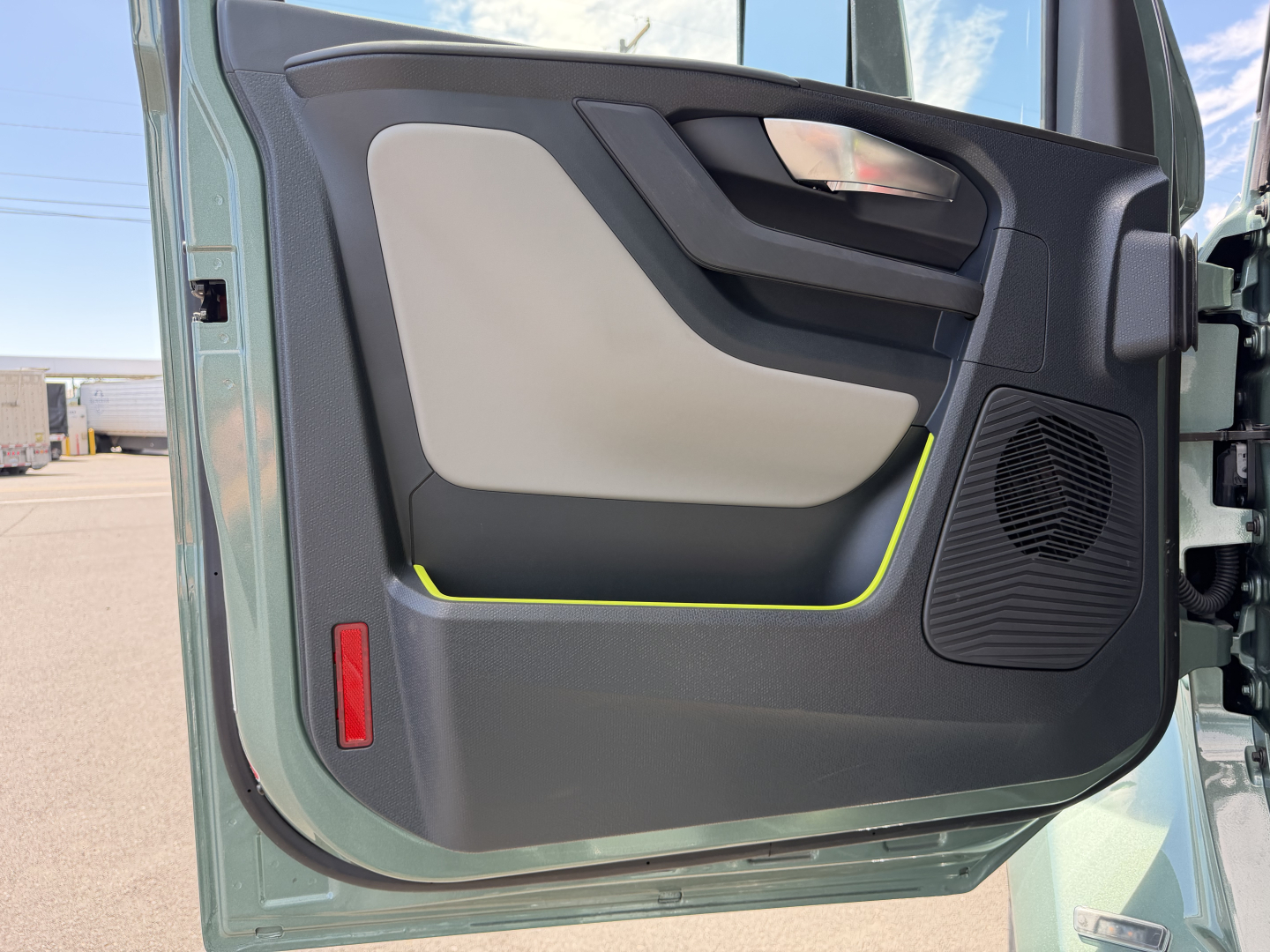 Volvo VNL64T860 door interior panel visible with beige and gray trim, black speaker grille, handle and yellow trim accent.