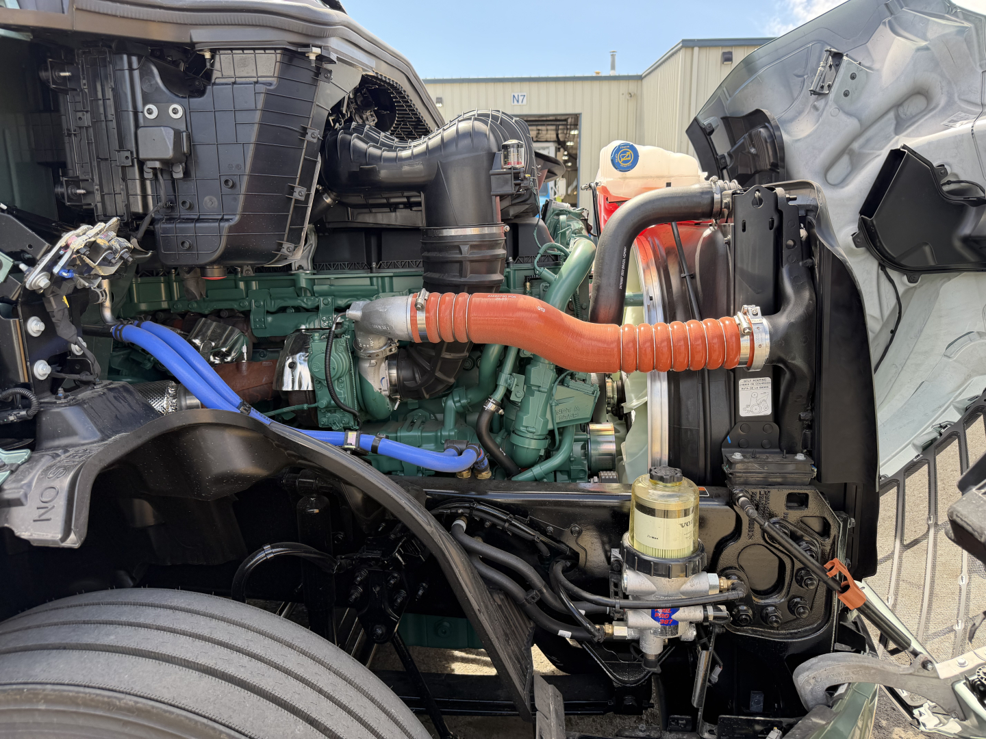 Volvo VNL64T860 engine bay showing green engine block, orange engine hose, blue hose, and diesel brackets in a truck with exposed components.