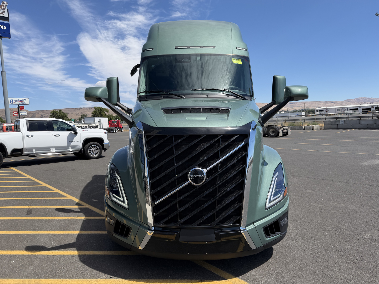 Front view of a Volvo VNL64T860 truck in teal green, with large grille, prominent Volvo emblem, aerodynamic bumper, and dual side mirrors.