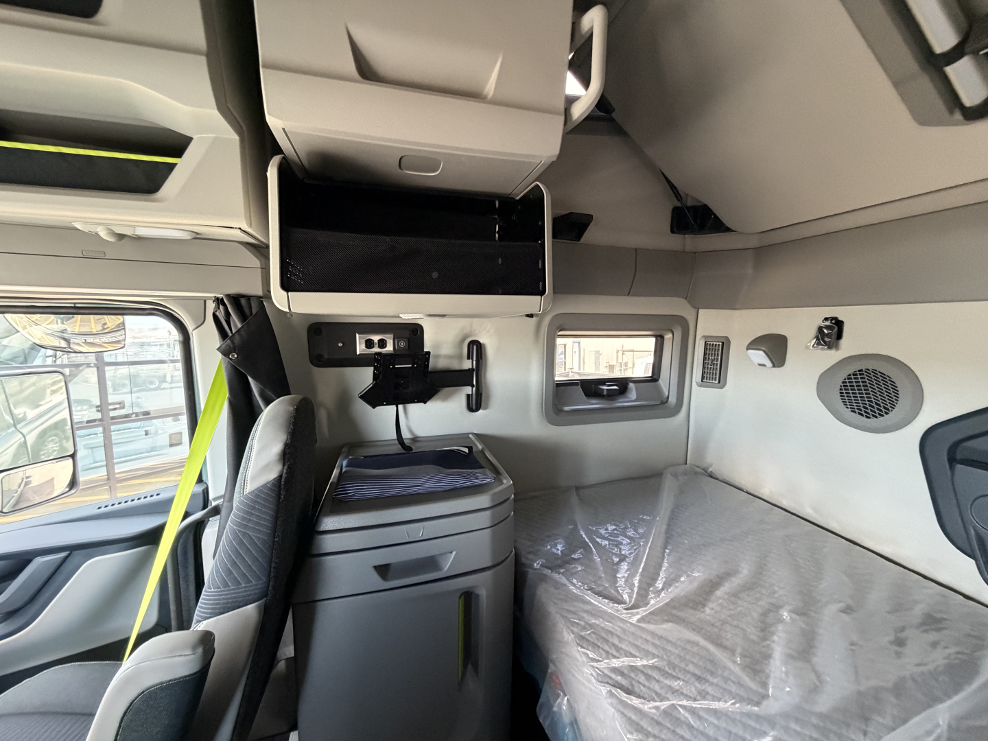 Volvo VNL64T860 sleeper cabin interior showing overhead monitor, storage cabinets, captain chair, and bed with plastic cover.
