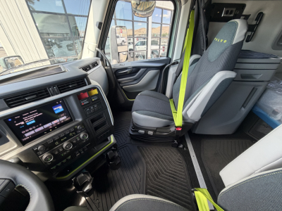 Volvo VNL cab interior showing steering wheel, dashboard with touchscreen, driver seat, passenger seat, and lime-green seat belts in a new truck.