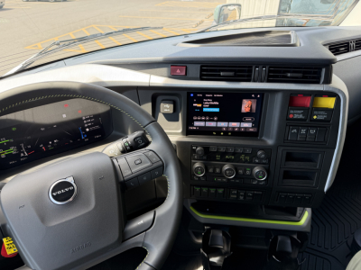 Dashboard and steering wheel of a Volvo VNL cab showing digital instrument cluster and infotainment screen, air vents, and control buttons.