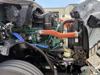 Volvo VNL64T860 engine bay showing green engine block, orange engine hose, blue hose, and diesel brackets in a truck with exposed components.