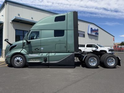 Volvo VNL64T860 green sleeper cab tractor viewed from side showing aerodynamic design, six-wheel rear, dealership building in background