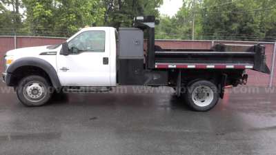 Ford F-450 dump truck with white cab and black dump bed side view showing drivetrain and rear wheels.