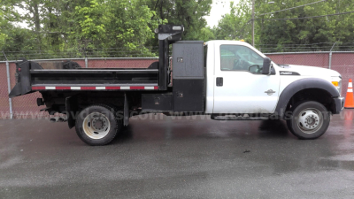 Ford F-450 dump truck side view showing dump bed and chassis with white cab and black utility compartments.