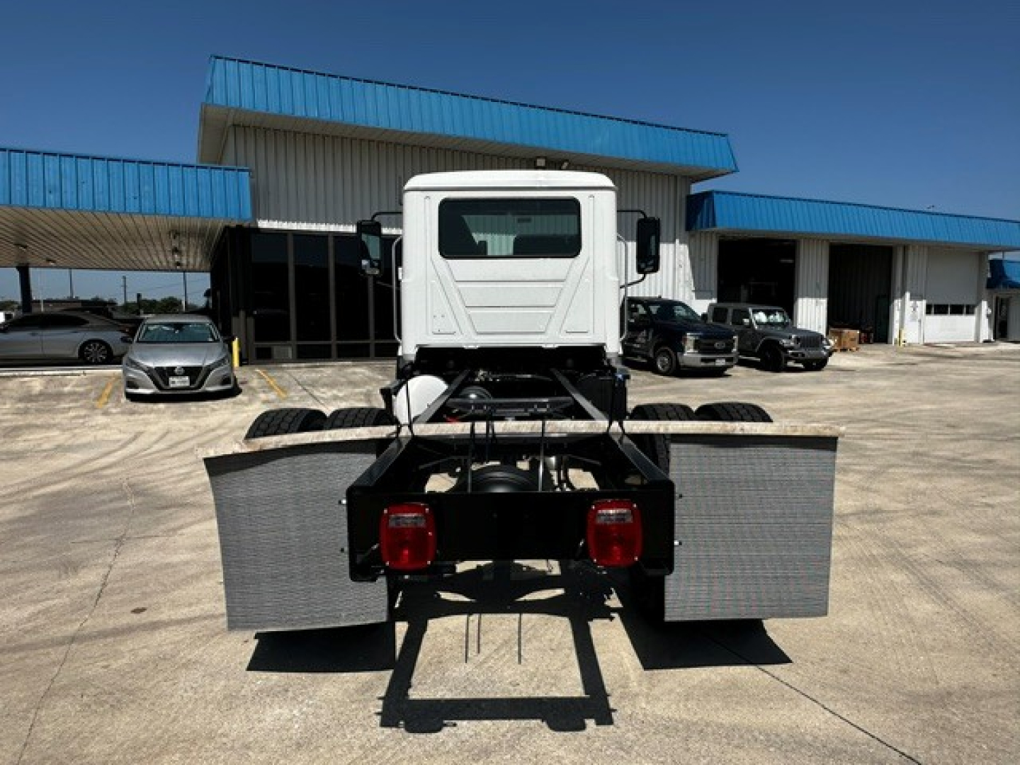 Truck chassis rear view showing cab and chassis with dual rear wheels and metal step/fenders.