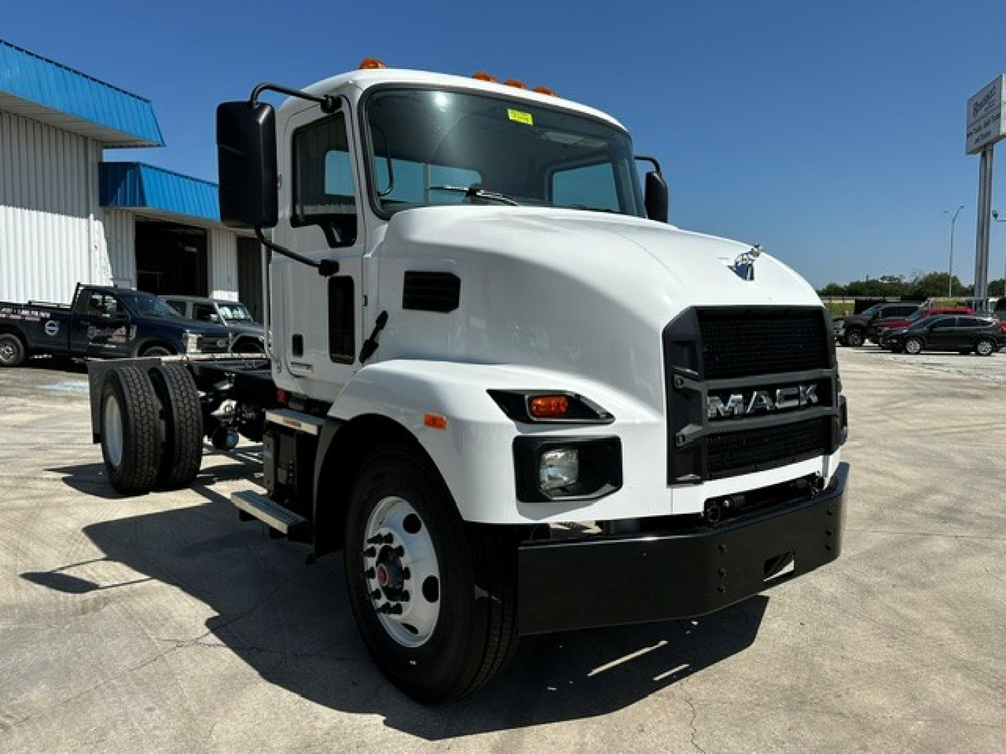 Mack MD6 cab and chassis truck front-left view showing white cab, black grille with MAC K letters, dual headlights, orange clearance lights, and heavy-duty bumper.