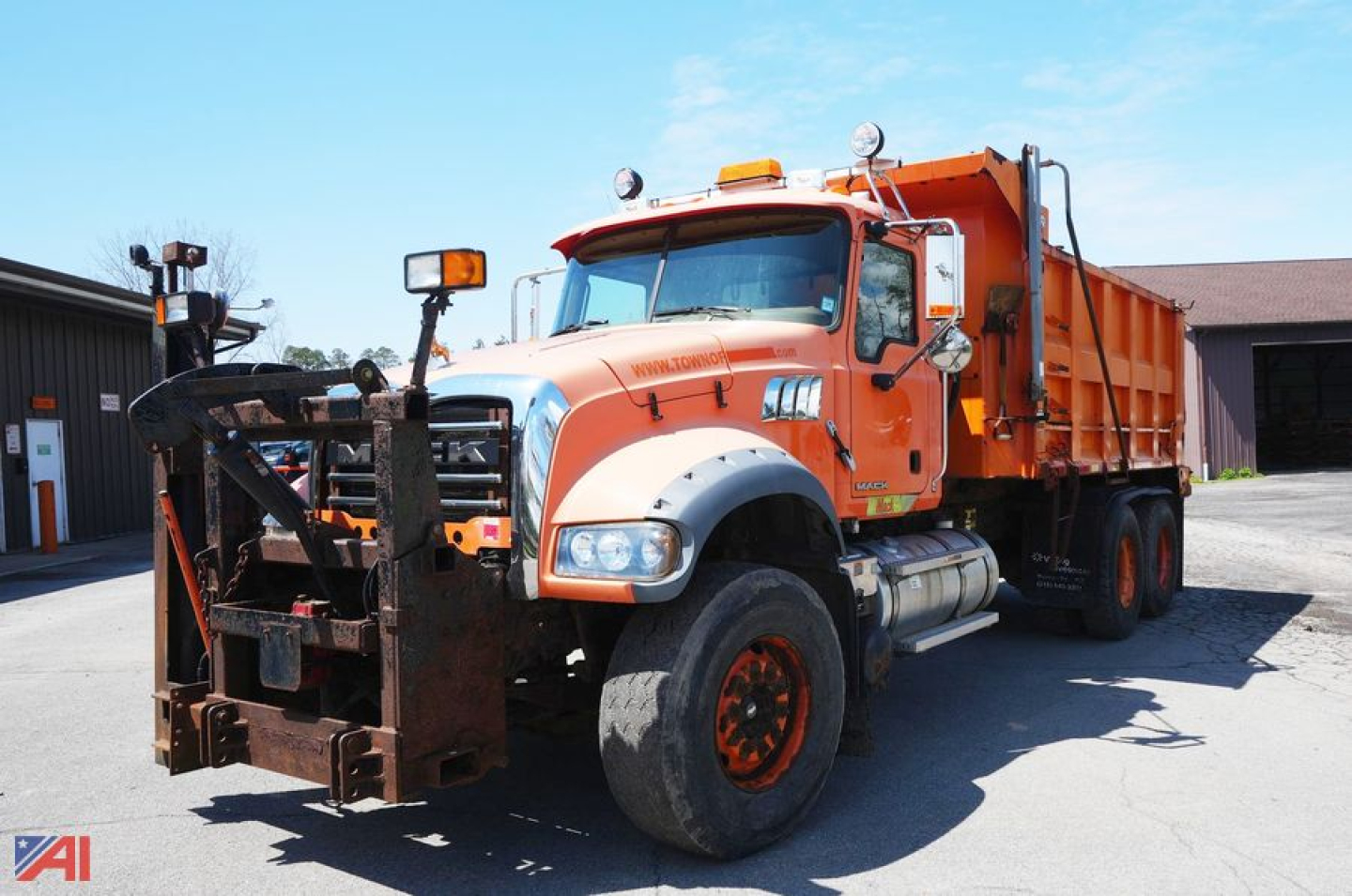 Orange and white 2009 Mack GU713 Granite dump truck with front bulldog-style hitch, large tires, and dump bed; auxiliary lights on cab roof; chrome mirrors; company yard.