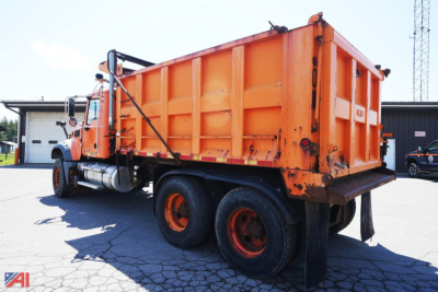 Orange Mack GU713 Granite dump truck with large rear dump bed and dual rear axles, side view showing orange body and black tires.
