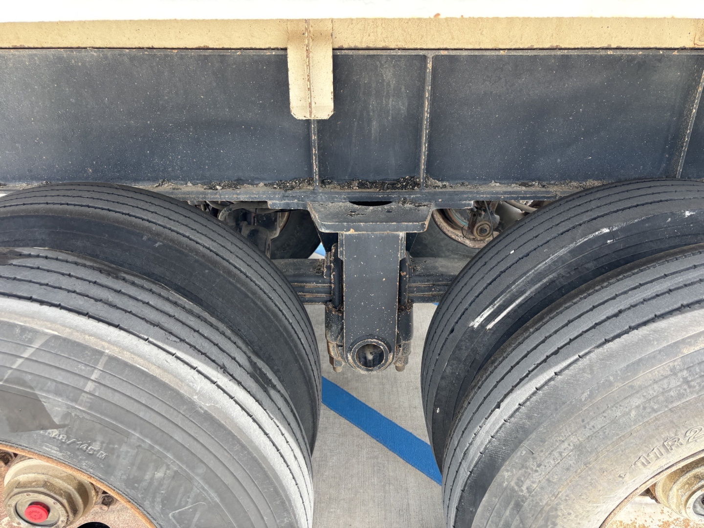 Dual rear axles with heavy-duty tires and suspension components of a dump trailer, chassis linkage and leaf spring area visible.