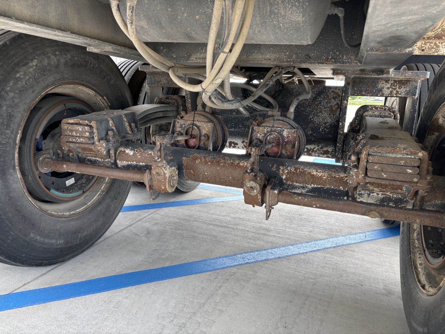 Trailer axle assembly showing leaf springs, differential hangers, and tires with rusted components.