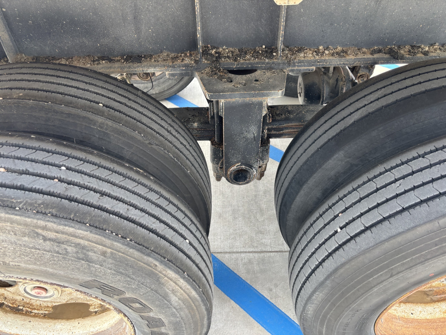 Trailer underside showing dual rear axles with heavy-duty tires and leaf spring suspension; hitch receiver and frame components visible.