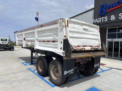 Trailer rear view showing white dump trailer with dual rear axles and black mud flaps. Visible text on mud flaps reads 'Brauners' or 'Bruchner' and tail lights; there are red and white reflective stripes along the sides.
