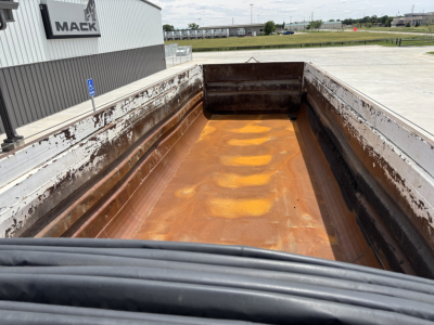 Dump trailer bed interior showing rusted metal walls and orange-brown bed surface, viewed from the front with sidewalls and tailgate edges.