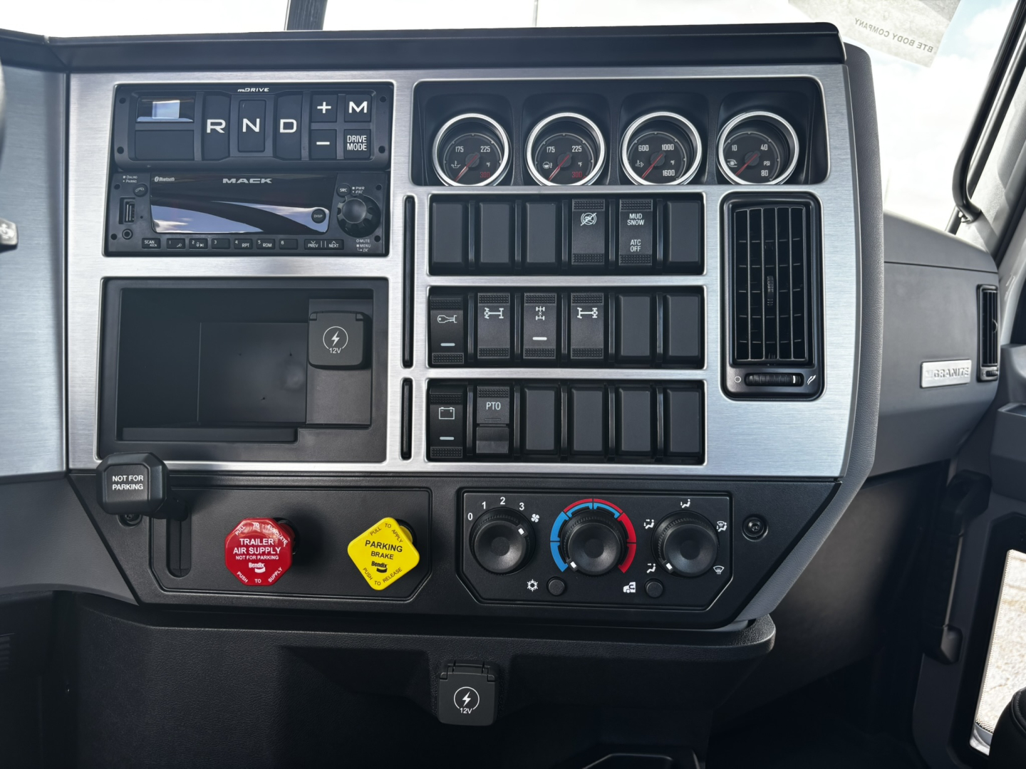 Cab interior of a Mack GR64FT truck showing dashboard gauges, infotainment, air controls, and ignition area.