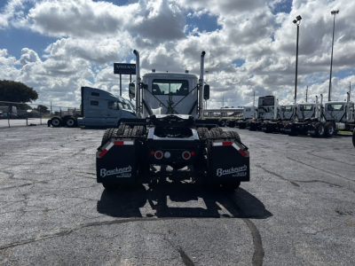 Rear view of a 2027 Mack GR64FT truck on a dealership lot, with sleeper cab, multiple trailers in background, and Brackner Fleet branding on mudflaps.