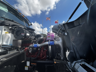Mack GR64FT engine bay view showing intake hoses, coolant reservoir, and engine components.