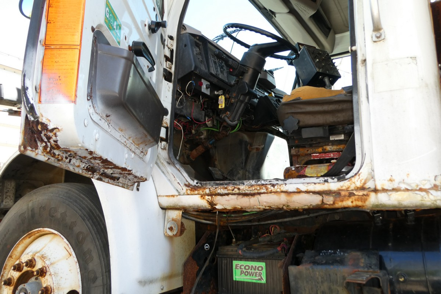 Truck cab interior exposed with steering wheel and dashboard visible; rusty steps and frame along door opening; ECONOPOWER label on battery area.