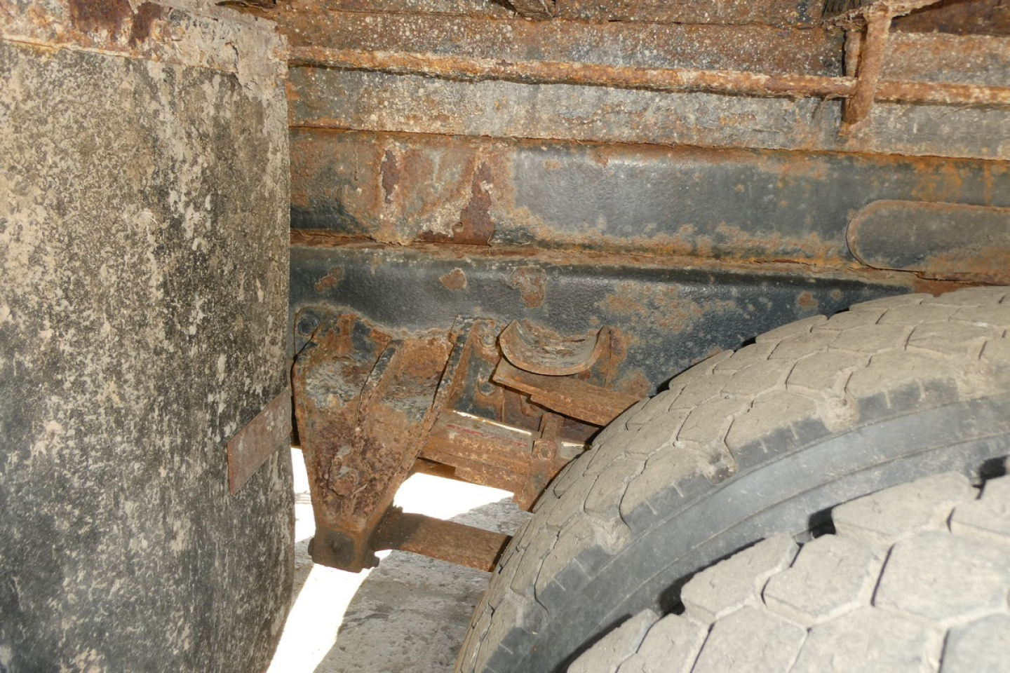 Dump truck undercarriage showing rusted frame rails and wheel with heavy wear.